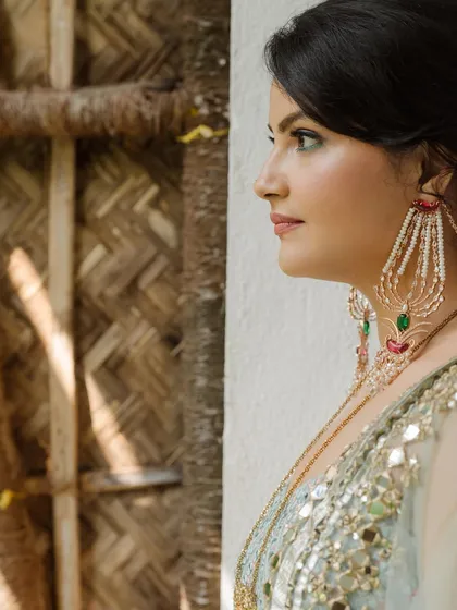 A profile of elegance. This portrait highlights the bride's stunning statement earrings and the intricate mirror work on her blouse, showcasing the detailed styling of her Mehendi look.
