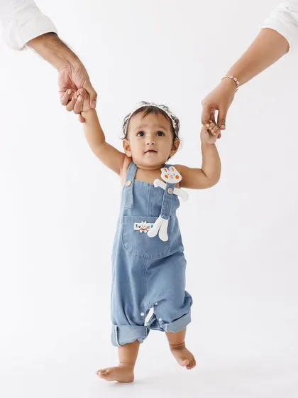 Guiding their little one's first steps. This milestone portrait captures a pivotal family moment, full of support, encouragement, and the excitement of a new chapter.