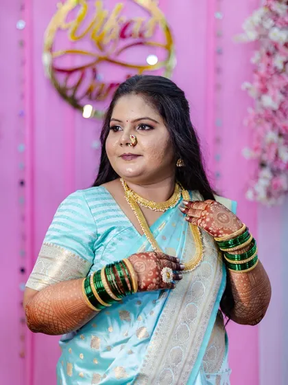 Adjusting her gold necklace, this bride-to-be looks absolutely regal. The makeup is balanced to complement the heavy gold jewelry and the rich fabric of her saree.