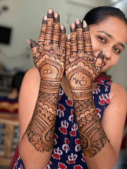 A happy client showing off her beautiful back-hand mehendi, which features her initial 'V' in a lovely script.