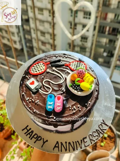 An anniversary cake for an active couple. This chocolate cake is topped with fondant decorations representing their shared hobbies, including badminton, fitness, and healthy eating.