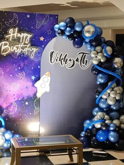 An outer space theme birthday party decoration. We used a galaxy-printed backdrop and a balloon arch in shades of deep blue, black, and silver, with astronaut and rocket ship elements to create a cosmic atmosphere.