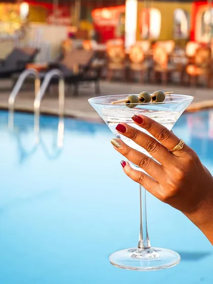 A woman's hand with festive nail polish holds a classic martini by the pool. This shot combines elegance with a relaxed, sun-drenched vacation vibe, perfect for a hotel or resort.