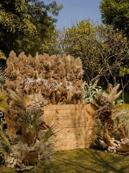 We traded classic florals for hay, pampas, and dried botanicals to create this bold, earthy aesthetic. The "You're The One" neon sign adds a modern, romantic touch to the sophisticated barnyard-chic setup.