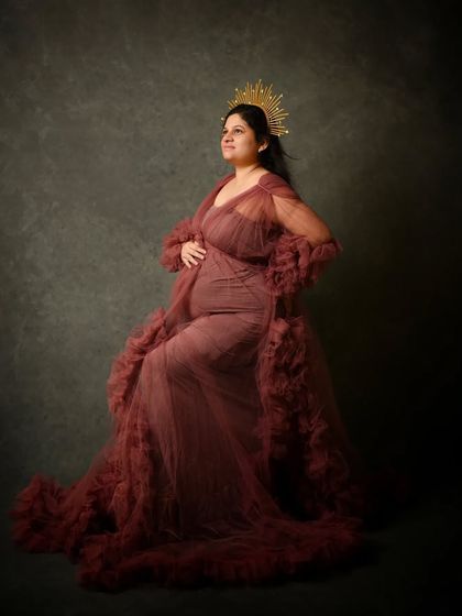 Seated gracefully, this mom-to-be looks like royalty in a ruffled gown and a golden sunburst headpiece, a popular prop from my collection.