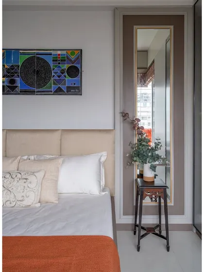 Details matter. A small, traditional-style stool serves as a unique bedside table, complemented by modern abstract art, showcasing our eclectic approach.