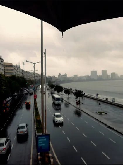 The view of Marine Drive, or the Queen's Necklace, from a foot-over bridge, framed by an umbrella. This classic perspective is made more moody and atmospheric by the rain.