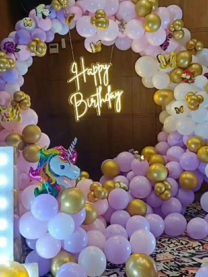 A magical unicorn-themed first birthday. This setup features a balloon ring in pastel purple, pink, and white, with gold and unicorn accents, a neon sign, and a light-up number '1'.