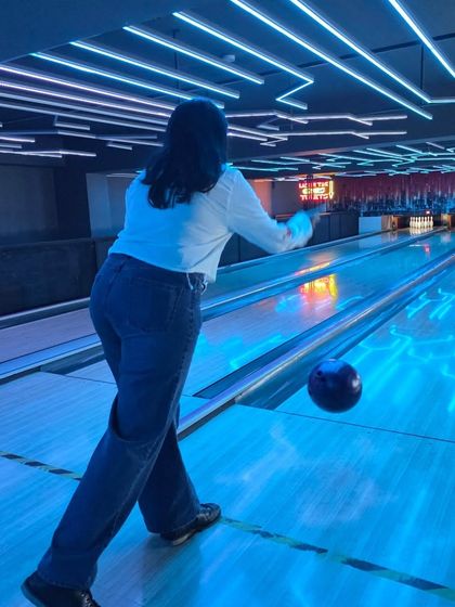 A player takes aim, with the bowling ball just moments from being released. The blue neon lights on the lane and ceiling create a cool, immersive effect.