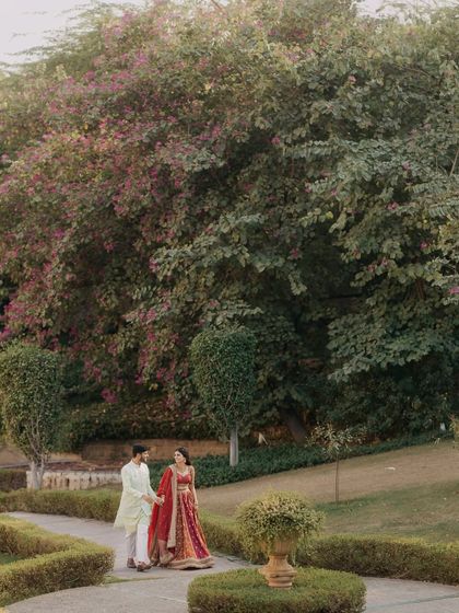 A wide shot of the couple taking a romantic stroll through a beautifully manicured garden, showcasing the grandeur of their wedding venue.