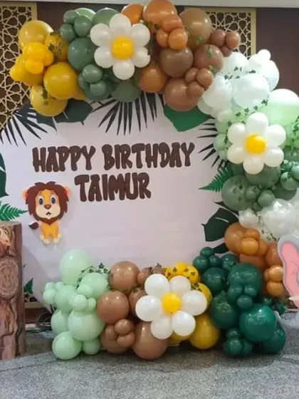 A cute jungle safari theme for Taimur's birthday. This circular backdrop is framed by a balloon garland in earthy tones, with adorable cutouts of a lion, giraffe, and elephant.