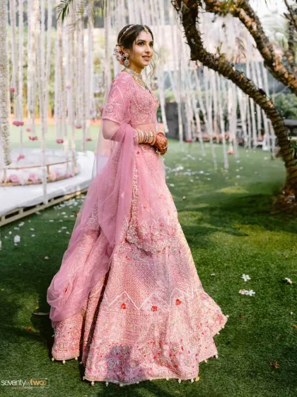 A full-length portrait of the bride in her stunning pink lehenga, captured in a garden setting, looking like a princess from a fairytale.