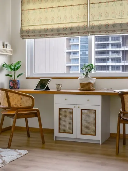 The 'Malhar' home office features a long window-side desk for two. The design incorporates a central storage cabinet with cane-fronted doors and is paired with matching rattan chairs.