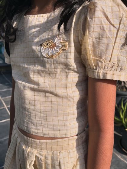 A timeless checkered two-piece set with a modern twist. The top features an adorable embroidered bird brooch and the flowy skirt has pretty golden details.