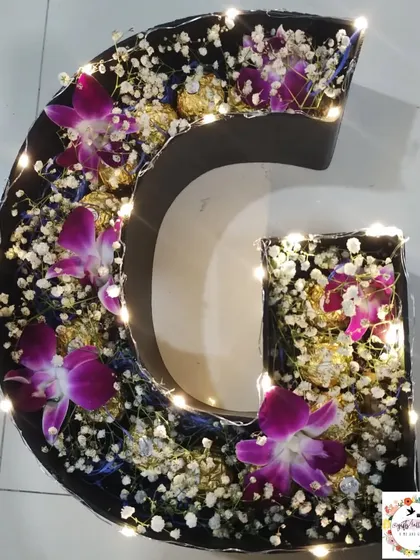 A unique twist on a traditional bouquet, this alphabet bouquet combines fresh flowers, Ferrero Rocher chocolates, and fairy lights inside a letter-shaped frame. This 'G' initial bouquet was designed for a special wedding occasion.