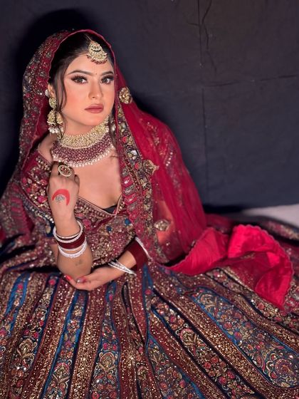 A full view of the bride in her magnificent red and blue lehenga. The hairstyle is a classic bridal bun that holds the dupatta securely.