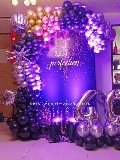A sophisticated 40th birthday decoration with a deep blue backdrop. The setup features a balloon arch in black, silver, and gold, with large foil number balloons.
