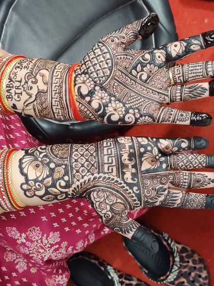 A detailed mehandi design for a baby shower. You can see the "Baby Girl" text and an elephant motif on the wrist, while the hands are covered in intricate traditional patterns.