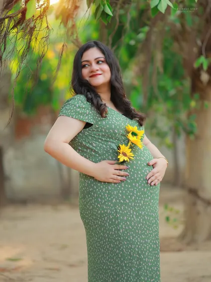 A beautiful solo portrait in a casual green dress, adorned with sunflowers. The warm sunlight highlights the mother-to-be's happy glow.