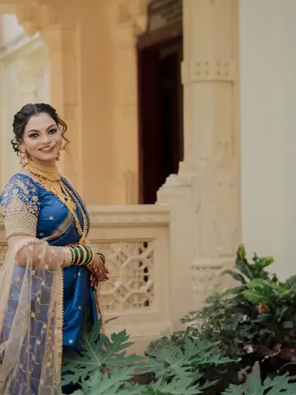 A lovely solo portrait of the bride in her blue Nauvari saree. Posed against a classic building, her confident and happy expression shines through.