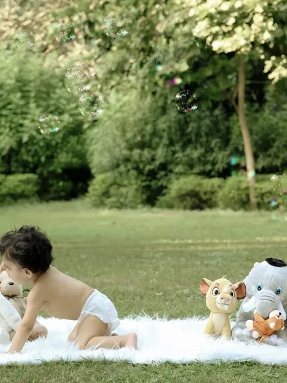 A baby crawls towards his lineup of stuffed animal friends during his outdoor shoot. This action shot captures a moment of playful interaction and movement.
