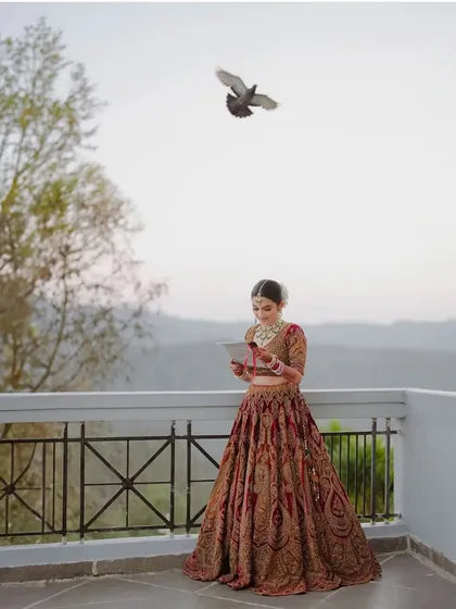 A breathtaking wide shot of the bride on the balcony. Her timeless look stands out beautifully against the vast mountain landscape, a truly cinematic moment.