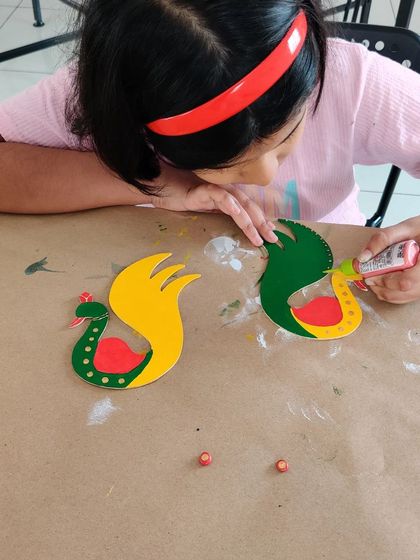 A close up of the crafting process. Using craft glue to add small, colorful dots is a fun detail that makes each handmade peacock T-light holder truly unique.