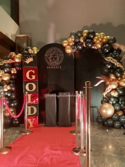A luxurious Versace-themed entrance with a red carpet, velvet ropes, and a black and gold balloon arch.
