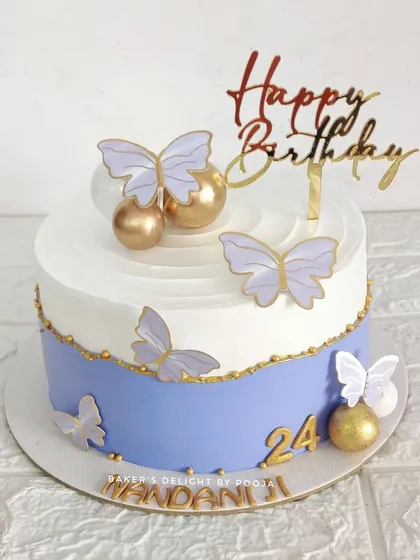 A beautiful butterfly-themed cake in a lovely lavender and white color scheme, accented with golden spheres.
