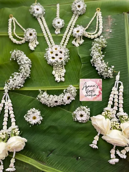 This is a full bridal Haldi jewellery set, handcrafted with white flowers, baby's breath, and pearls. The complete collection includes a necklace, earrings, maang tikka, bajuband (armlets), hath phool (hand harnesses), and matching floral kaliree.