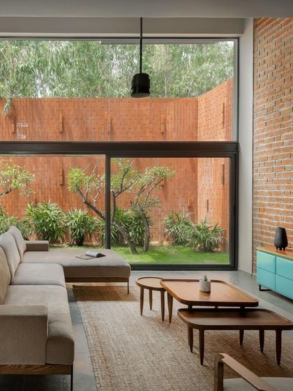 A view of the living room, where the neutral sofa and jute rug are contrasted by a pop of turquoise in the console. The exposed brick wall adds warmth and texture, while the large window frames the garden like a living piece of art.