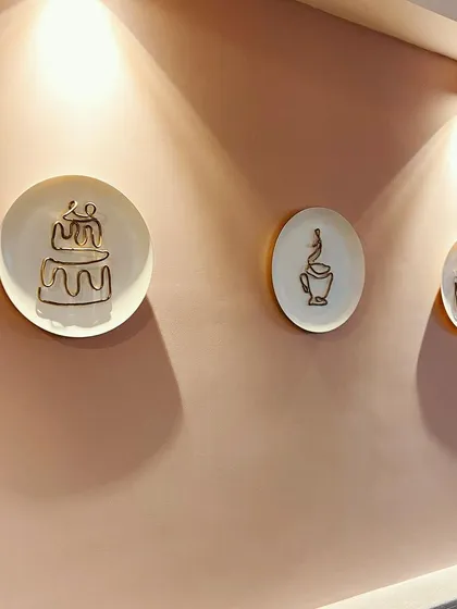 This installation was designed for a cafe wall, featuring minimal wire sculptures of a cake and coffee cup mounted on plates. The simple gold wire against the plain plates creates an elegant and modern look, perfectly complementing the cafe's aesthetic.