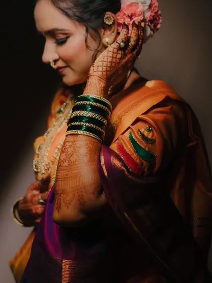 A close-up focusing on the details: the bride's intricate henna, green glass bangles, and the floral arrangement in her hair.