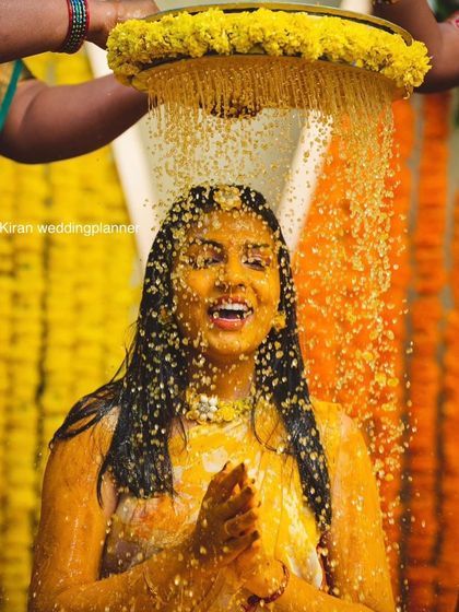 A joyful moment from a Haldi ceremony, where the bride is being showered with turmeric-infused water and flower petals.