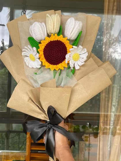 Taking a picture of the sunflower and tulip bouquet against a window. The natural light highlights the texture and colors of the yarn.