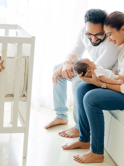 A lifestyle shot of new parents admiring their baby in a white crib.