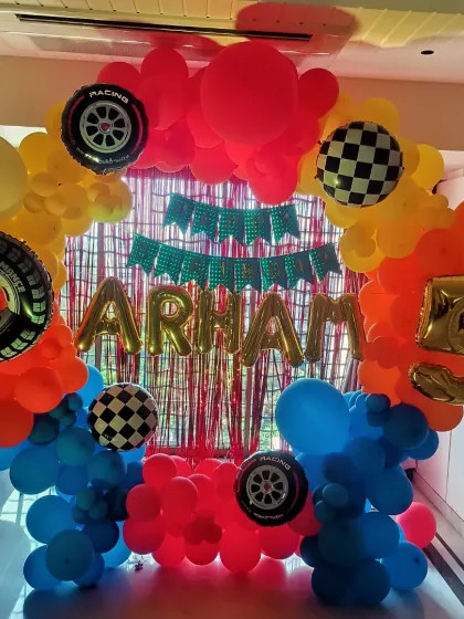 Get ready to race with a Hot Wheels theme! This colorful room decoration includes a balloon ring with tire and checkered flag accents, a red foil curtain, and the birthday boy's name in gold foil letters.
