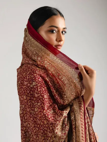The model draped in a rich maroon saree, giving a regal and mysterious vibe. The smokey eye makeup adds to the drama of the shot.