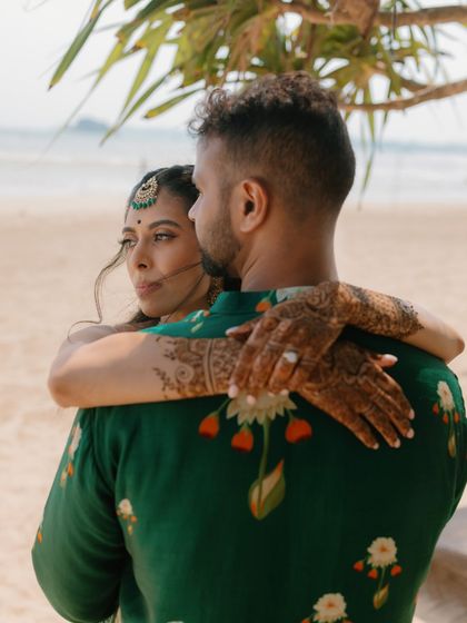 An intimate embrace on a Sri Lankan beach. The focus is on the bride's henna-adorned arms around the groom, her gaze looking thoughtfully into the distance, creating a poetic and beautiful portrait.