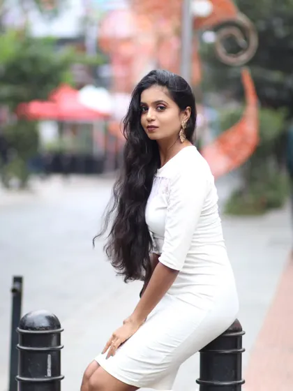 A classic portrait pose, seated on a bollard. The shallow depth of field separates the model from the busy street background.