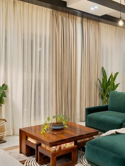 A cozy corner in an industrial-style living room. The combination of sheer and heavy curtains softens the space, while the emerald green sofa and solid wood coffee table provide a rich, textured feel.