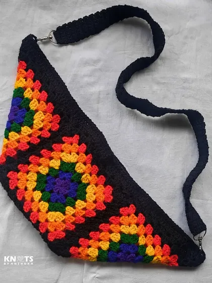 A full view of the rainbow granny square crossbody bag, showing its unique triangular shape and adjustable strap.