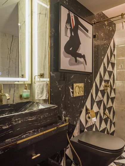 A powder room with a bold black and white theme. The design features a black marble sink, geometric floor tiles, and quirky modern art.