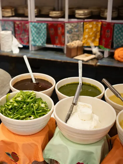 The essential components of great Indian food. Bowls of tangy tamarind chutney, fresh green chutney, spicy chilies, and creamy yogurt, ready to accompany our delicious snacks.
