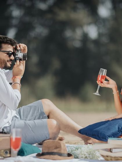 A candid moment from a vintage-themed picnic on the beach. The props, like an old camera and radio, add a nostalgic charm to the scene.