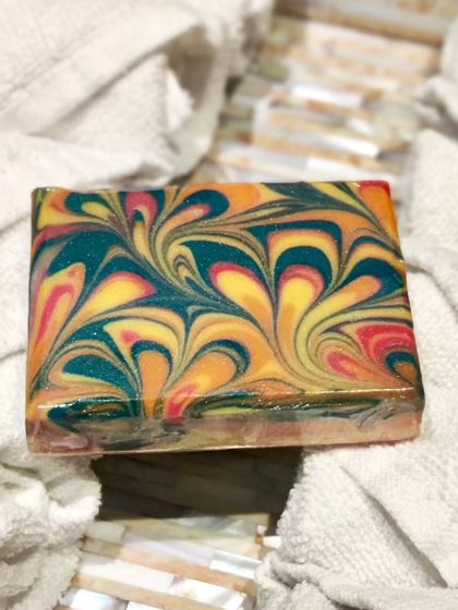 This peacock swirl soap is a feast for the eyes, with rich jewel tones of teal, yellow, and magenta. It's a complex pour that results in a stunning, feather-like design.