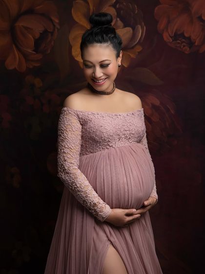 A quiet moment of reflection. This close-up portrait showcases the delicate lace details of the gown and the beautiful, gentle smile of an expecting mother against a painterly floral background.