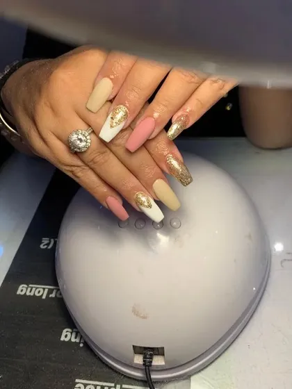 A glamorous set of coffin nails with a mix of matte pink, matte beige, and full-coverage gold glitter and chrome.