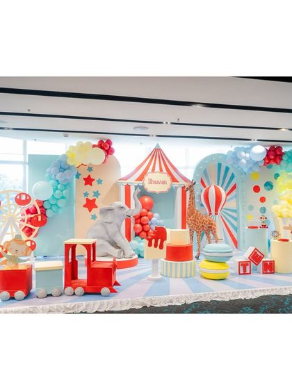 A grand circus stage setup, complete with a red-and-white striped big top, a Ferris wheel, a circus train, and life-sized elephant and giraffe props.