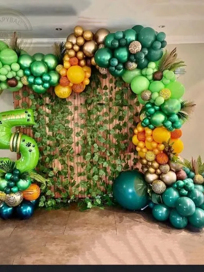 An organic balloon arch designed to look like a lush jungle vine. I used various shades of green, gold, and orange balloons, along with a large number '5' foil balloon, against a bamboo-style backdrop.